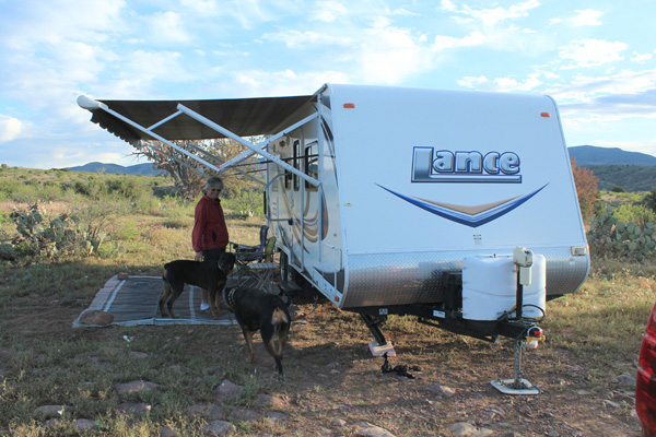 Linda, our dogs, and our trailer at our dispersed campsite in morning light.