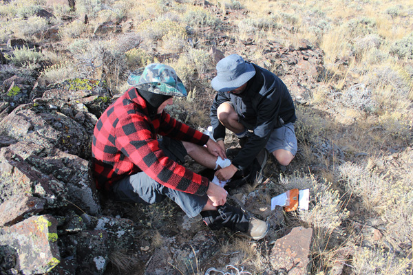 Michael and John clean and bandage Michael's leg injury on Mickey Butte's summit.