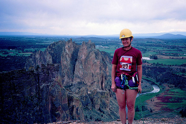 Linda at the top of Monkey Face. The Smith Rock Group of cliffs, the Crooked River, and the Oregon Cascades lie behind her.